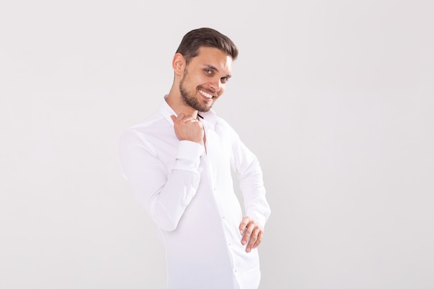 Retrato de joven guapo feliz en camisa casual de pie contra la superficie blanca con