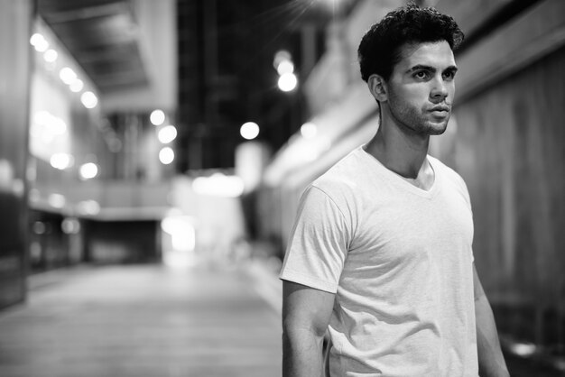 Foto retrato de joven guapo hispano explorando las calles de la ciudad por la noche