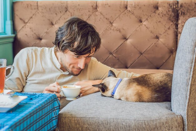 Retrato de joven guapo jugando con gato y bebe café