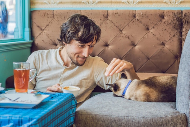 Retrato de joven guapo jugando con gato y bebe café.