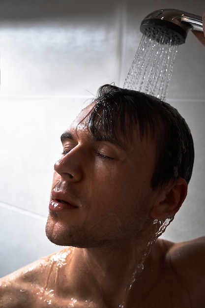 Foto retrato de joven guapo se lava con gel de ducha, hace espuma la cabeza con champú en el baño en casa de cerca