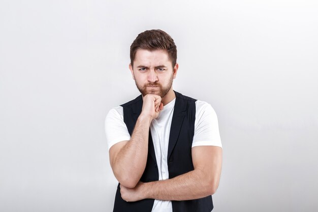 Retrato de joven guapo morena pensativa en camisa blanca sobre fondo gris. el chico piensa