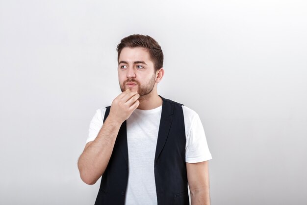 Foto retrato de joven guapo morena pensativa en camisa blanca sobre fondo gris. el chico piensa