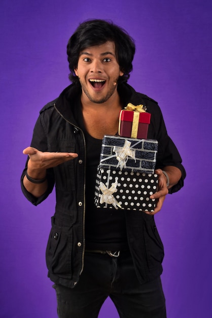 Retrato de un joven guapo sonriente feliz sosteniendo una caja de regalo en un fondo morado