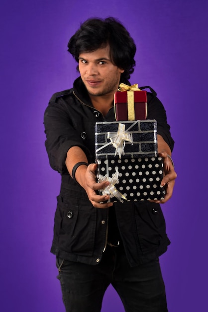 Retrato de un joven guapo sonriente feliz sosteniendo una caja de regalo en un fondo morado