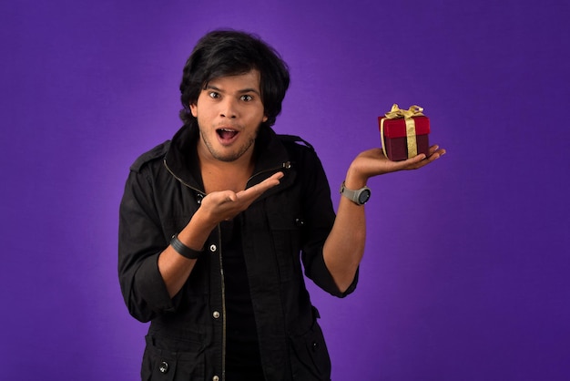 Retrato de un joven guapo sonriente feliz sosteniendo una caja de regalo en un fondo morado