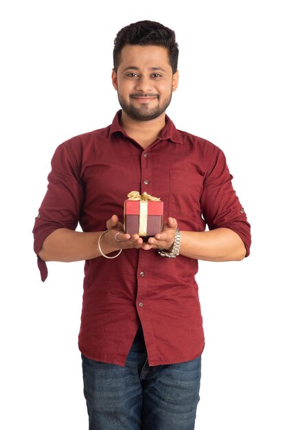 Retrato de un joven guapo sonriente feliz sosteniendo una caja de regalo y posando sobre un fondo blanco