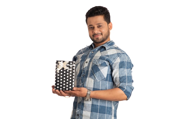 Retrato de un joven guapo sonriente feliz sosteniendo una caja de regalo y posando sobre un fondo blanco