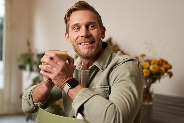 Retrato de un joven guapo con una taza de café sentado en una silla en una cafetería sonriendo y relajándose