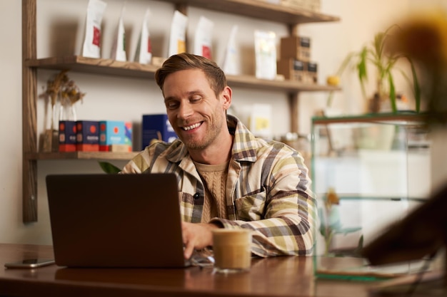 Retrato de un joven guapo usando una computadora portátil en un café sentado con una computadora en un espacio público creativo