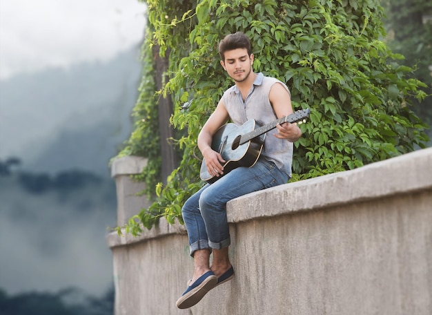 Retrato de un joven guitarrista sentado en el parapeto y mirando a la cámara