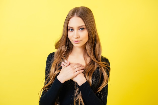 Retrato de joven y hermosa atractiva linda (adolescente colegiala) modelo de mujer con cabello largo toma de la mano por el corazón sobre fondo amarillo en estudio