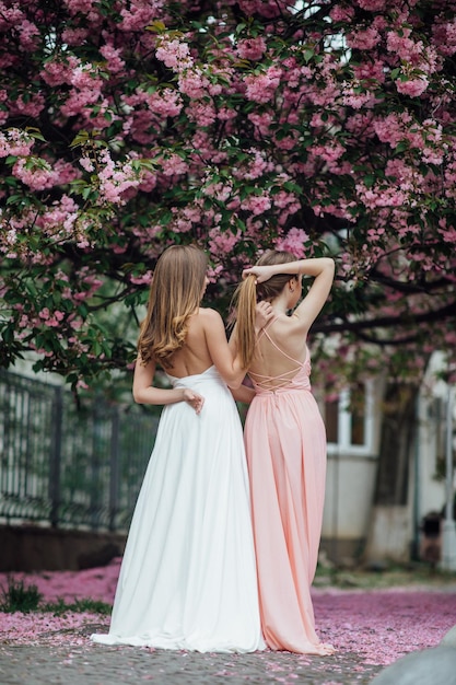 Retrato de joven hermosa chica de moda posando cerca de un árbol floreciente con flores rosas.