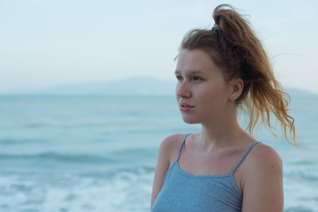 Retrato joven hermosa chica en el terraplén de fondo con vista al mar y la isla sonriendo relajándose con los ojos cerrados puesta de sol respiración profunda aire fresco