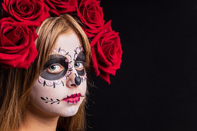 Retrato de joven hermosa con esqueleto de maquillaje en la cara y rosas rojas en la cabeza