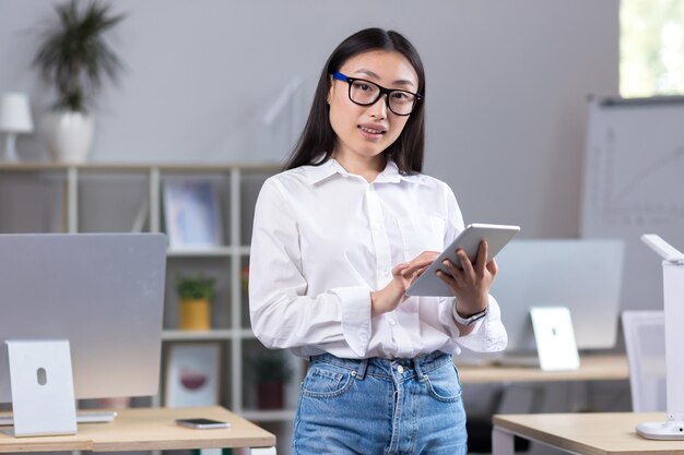 Retrato de una joven y hermosa estudiante asiática con gafas, camisa blanca y jeans de pie en el