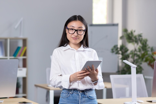 Retrato de una joven y hermosa estudiante asiática con gafas, camisa blanca y jeans de pie en el