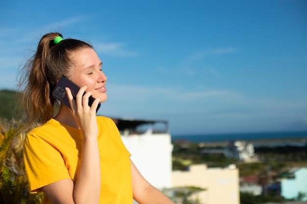 Retrato de una joven hermosa y feliz mujer positiva está hablando por su teléfono celular llamando a un teléfono inteligente en un día soleado de verano en el fondo del cielo disfrutando de una conversación con un amigo