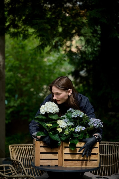 Retrato de una joven hermosa florista abrazando un ramo de hermosas flores en una olla de madera sobre la mesa en el jardín