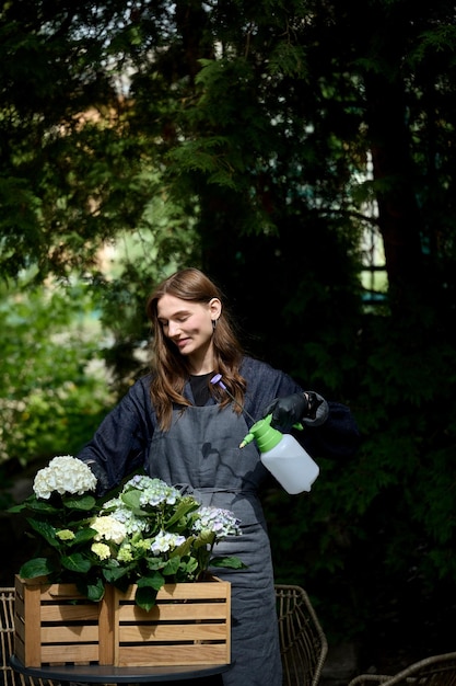 Retrato de una joven hermosa florista en un delantal regando plantas en una olla en el jardín