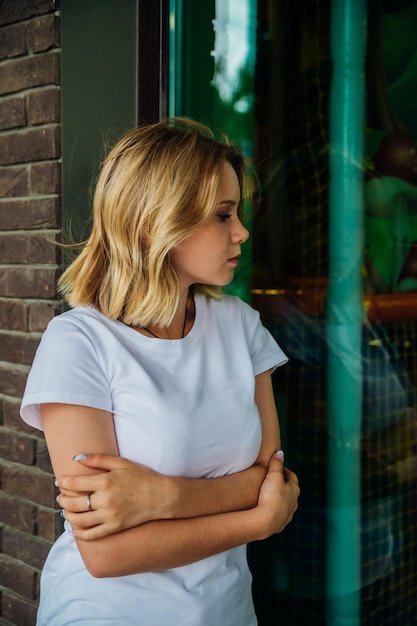 Retrato de una joven hermosa mirando a la cámara contra una pared de ladrillos. Una adolescente de moda con ropa informal de verano. Su cabello se lo lleva el viento y le cae sobre la cara.