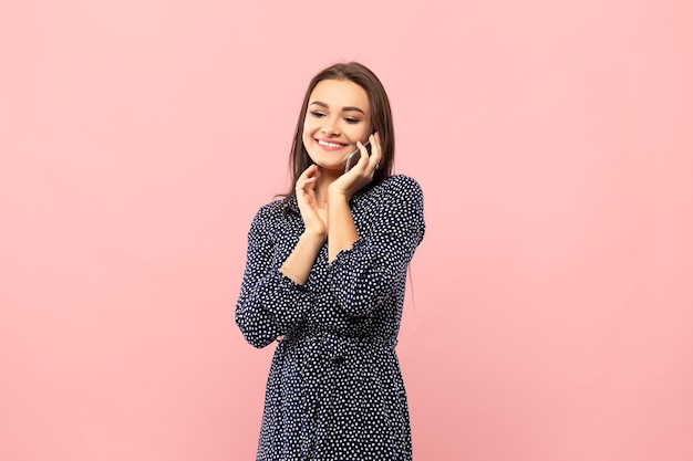 Retrato de una joven hermosa mujer aislada de fondo rosa con un vestido azul de lunares Una atractiva chica sonriente habla por teléfono móvil