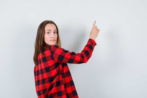 Foto retrato de joven hermosa mujer apuntando hacia arriba en camisa casual y mirando confiado