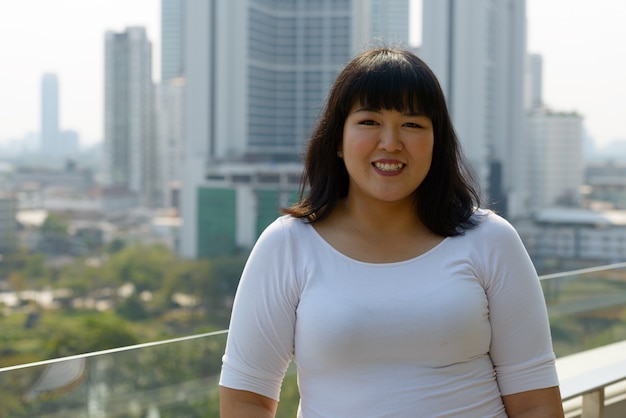 Retrato de joven hermosa mujer asiática con sobrepeso contra la vista de la ciudad