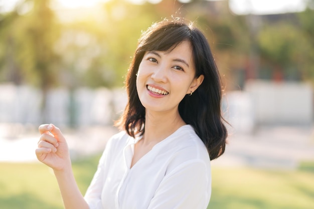 Foto retrato joven hermosa mujer asiática con sonrisa feliz alrededor del parque al aire libre en un día soleado de verano