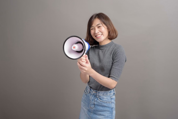 Un retrato de una joven y hermosa mujer asiática sosteniendo un megáfono sobre el fondo del estudio.