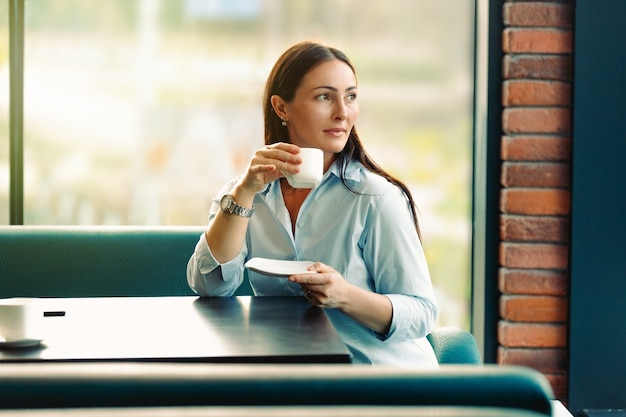 Retrato de joven hermosa mujer bebiendo té y mirando con una sonrisa mientras disfruta de su tiempo libre, agradable mujer de negocios en la cafetería moderna durante su descanso de trabajo.