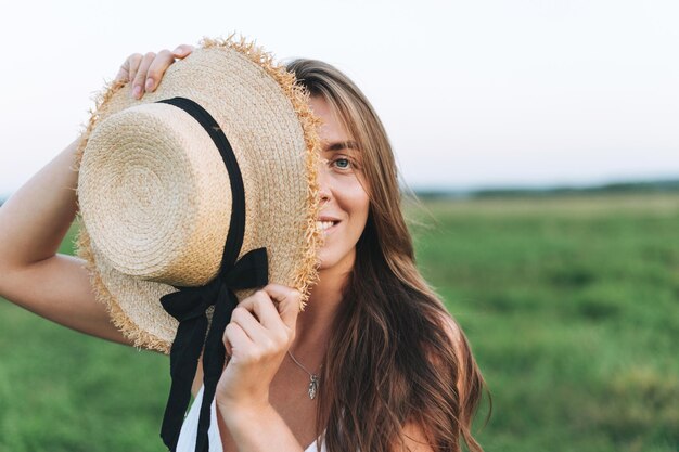 Retrato de joven hermosa mujer de cabello largo despreocupada en vestido blanco con sombrero de paja en el campo de la puesta del sol Sensibilidad al concepto de naturaleza