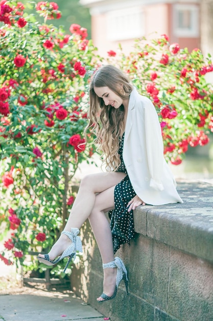 Retrato de una joven y hermosa mujer delgada de pelo largo con un romántico vestido blanco y negro cerca de una rosa roja floreciente en el centro de una ciudad europea Modelo de 23 años con ropa clásica Verano