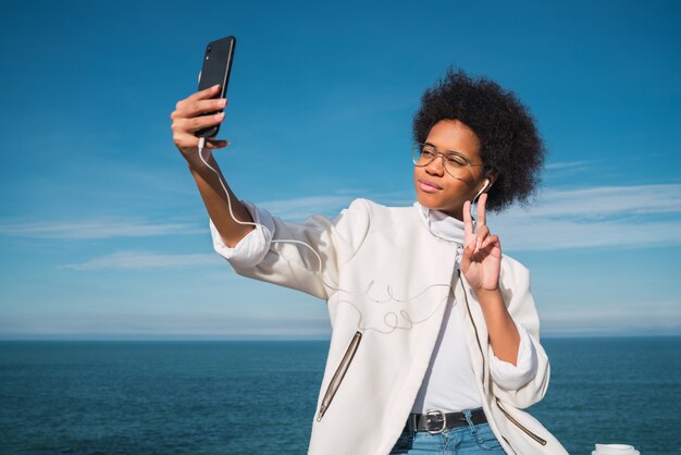 Retrato de joven hermosa mujer latina tomando selfies con su teléfono móvil al aire libre con el mar