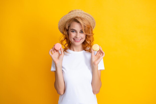 Retrato de joven hermosa mujer con macarrones Macaron francés Chica disfrutando de dulces aislados sobre fondo amarillo