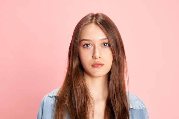 Retrato de una joven hermosa mujer mirando a la cámara con una expresión tranquila y seria contra el rosa