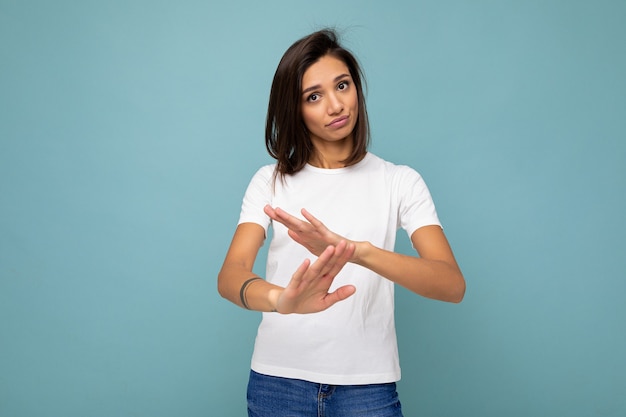 Retrato de joven hermosa mujer morena con emociones sinceras con camiseta blanca de moda para maqueta aislada sobre fondo azul con espacio vacío y mostrando gesto de tiempo de espera.