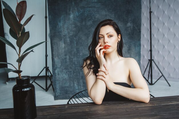 Retrato de una joven hermosa mujer morena sentada en una mesa sobre un fondo de espacio de copia gris oscuro