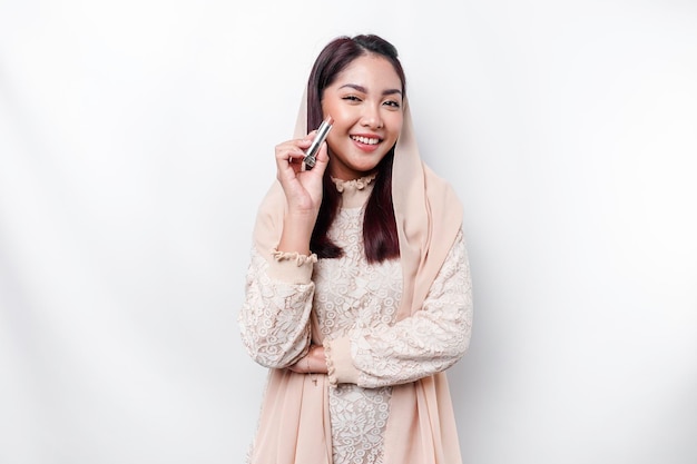 Retrato de una joven y hermosa mujer musulmana asiática con un pañuelo en la cabeza sosteniendo su pintalabios
