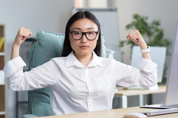 Retrato de una joven y hermosa mujer de negocios asiática que muestra con sus propias manos que es fuerte