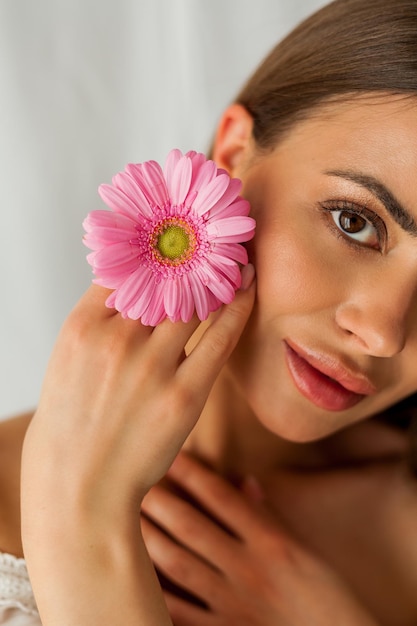 Retrato de joven hermosa mujer de ojos marrones de pelo largo con gerbera rosa sobre fondo blanco Vacaciones de primavera Día de la madre