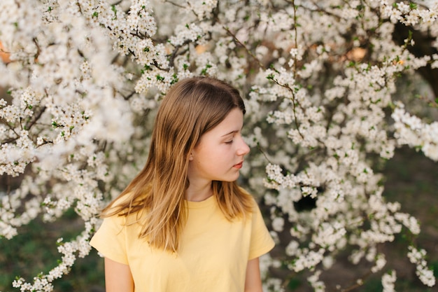 Retrato de joven hermosa mujer rubia cerca de árbol floreciente con flores blancas en un día soleado.