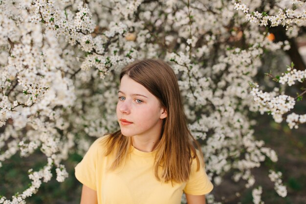 Retrato de joven hermosa mujer rubia cerca de árbol floreciente con flores blancas en un día soleado.