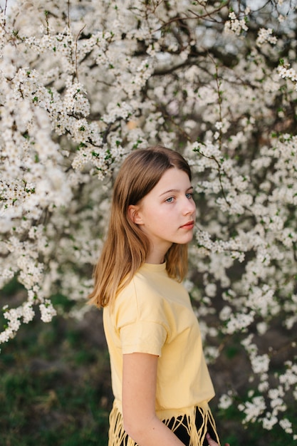 Retrato de joven hermosa mujer rubia cerca de árbol floreciente con flores blancas en un día soleado.