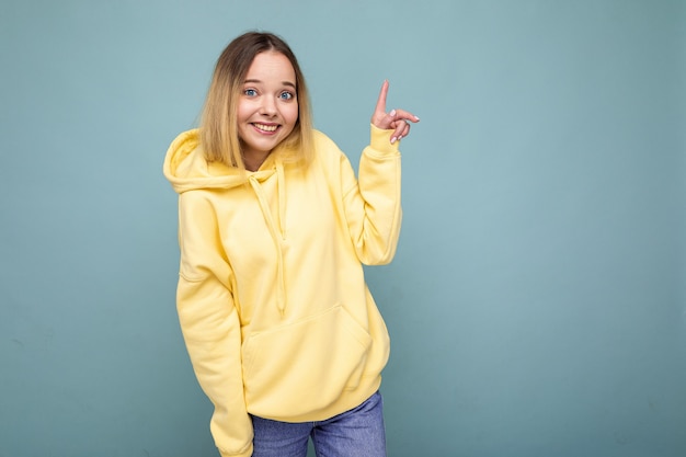 Retrato de joven hermosa mujer rubia hipster sonriente en moda sudadera con capucha amarilla sexy despreocupado