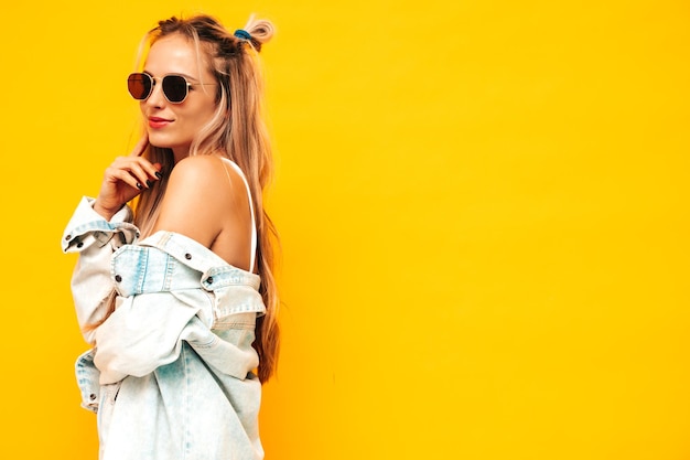 Retrato de joven hermosa mujer rubia sonriente en ropa de verano de moda Mujer despreocupada sexy posando junto a la pared amarilla en el estudio Modelo positivo divirtiéndose en el interior Alegre y feliz en gafas de sol