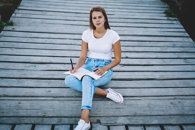 Foto retrato de joven hermosa mujer sentada al aire libre con bloc de notas encantadora chica hipster en jeans