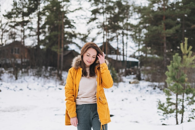 Retrato de joven hermosa mujer sonriente en chaqueta amarilla caminando en el bosque de invierno
