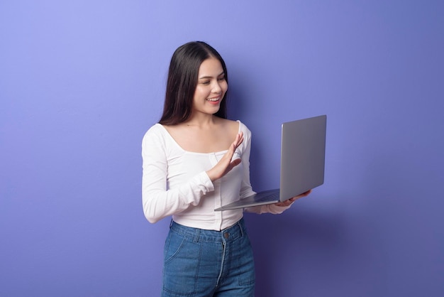 Un retrato de una joven hermosa mujer sonriente sostiene una laptop sobre un estudio aislado de fondo morado