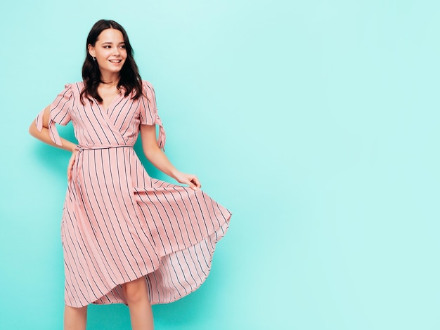 Foto retrato de joven hermosa mujer sonriente en vestido rosa de verano de moda mujer sexy despreocupada posando cerca de la pared azul en el estudio modelo positivo divirtiéndose en el interior alegre y feliz